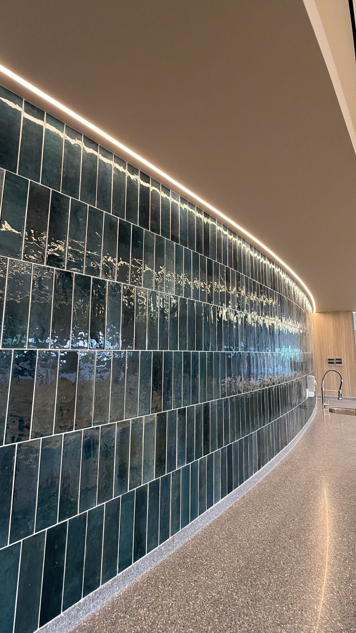 Continuous linear light following a curved tiled wall in a circulation space